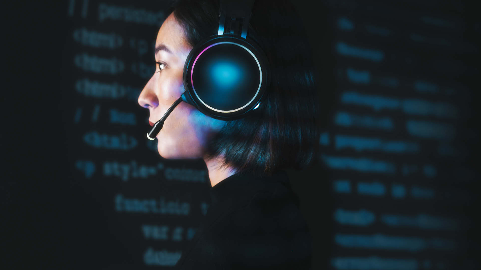 Woman wearing headset in front of computer screen displaying code.