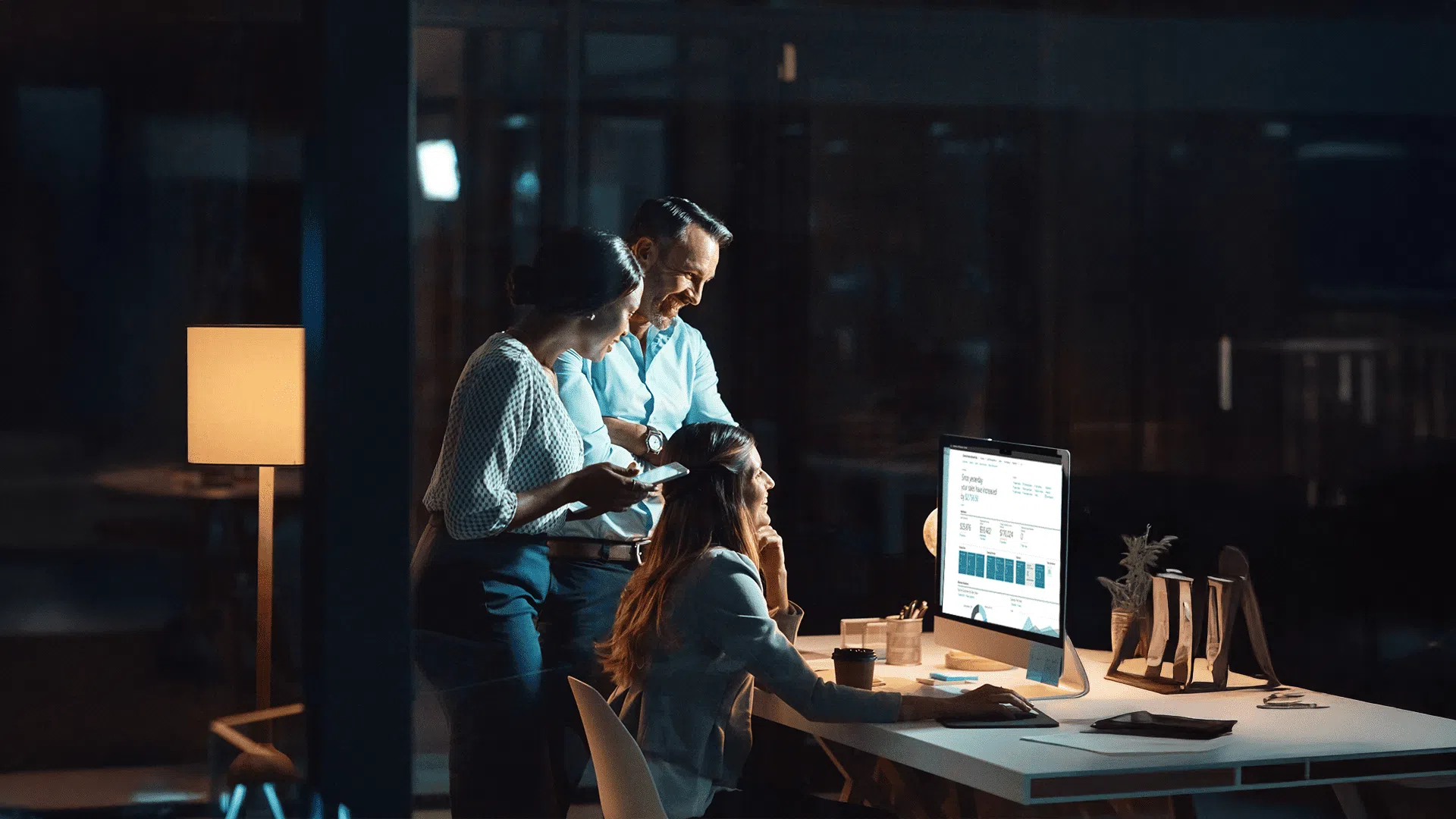 Three colleagues collaborating on a computer at night in an office.