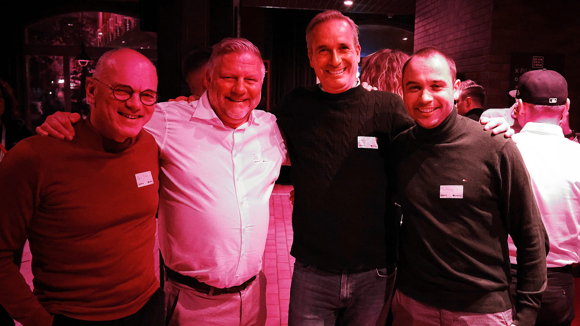 Vier Männer in Freizeitkleidung auf einem Event, lächelnd in einer Bar.