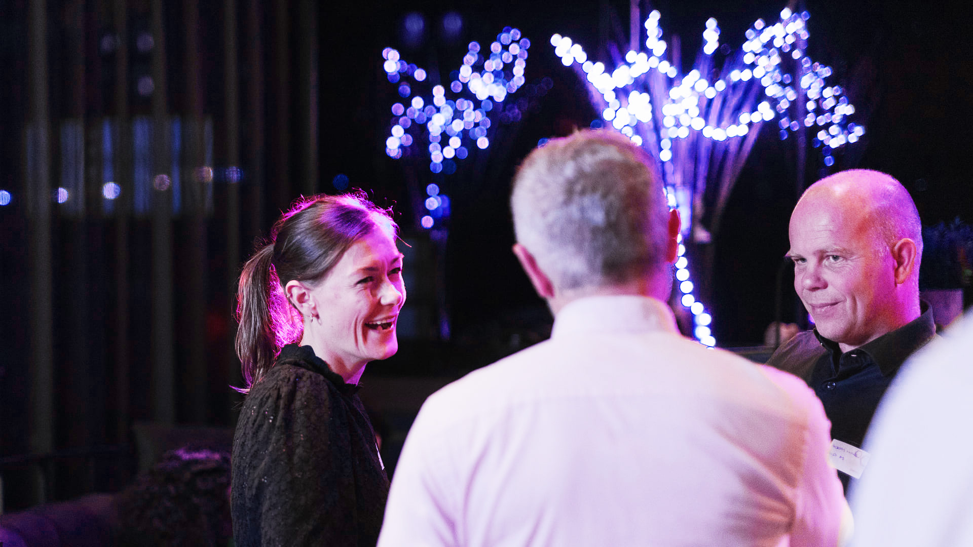 Drei Personen im Gespräch bei einer Veranstaltung mit lila Beleuchtung.