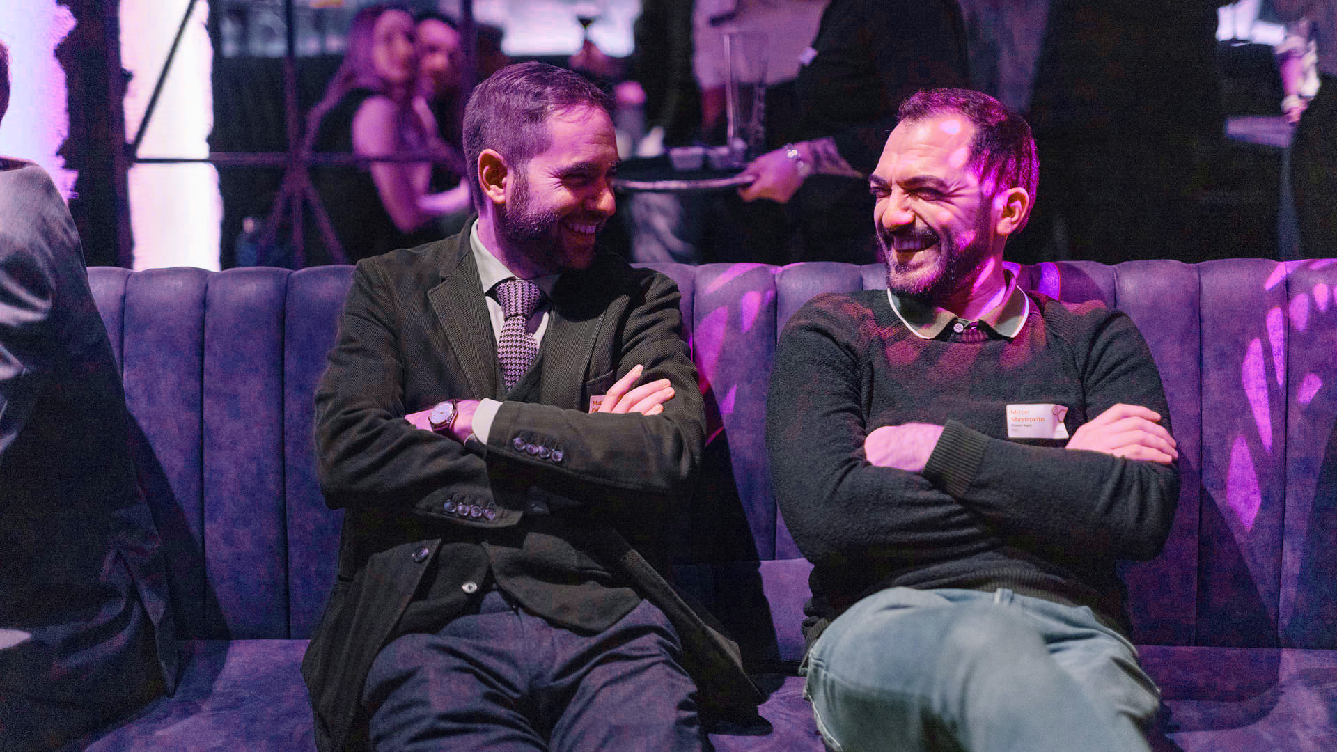 Zwei Männer lächelnd auf einem Sofa bei einer Veranstaltung.