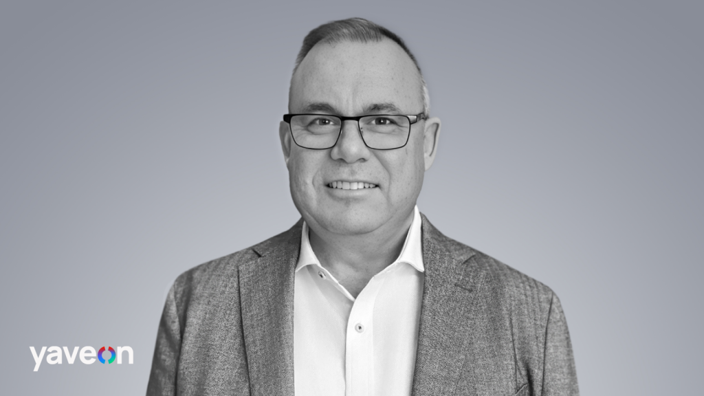 Portrait of a man with glasses and a gray blazer against a gray background.