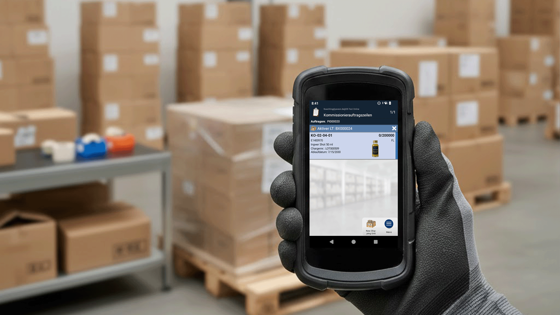 Hand hält Gerät in Lager mit Stapeln von Kartons.