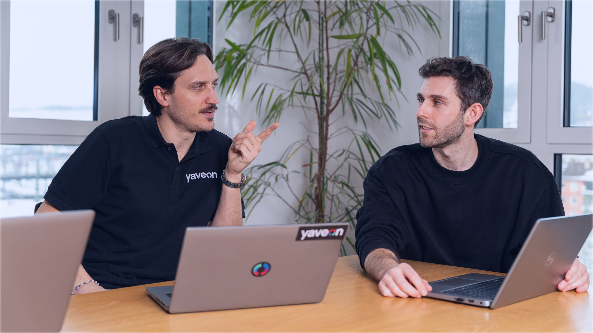 Zwei Männer unterhalten sich im Büro mit Laptops am Tisch.