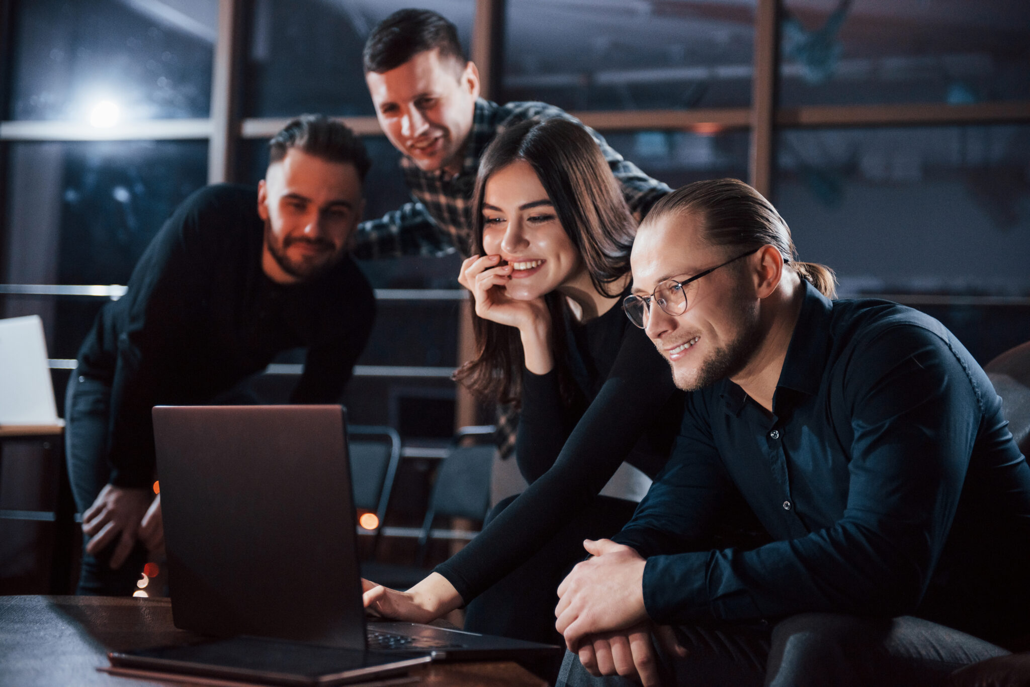 Group of four people smiling at a laptop.
