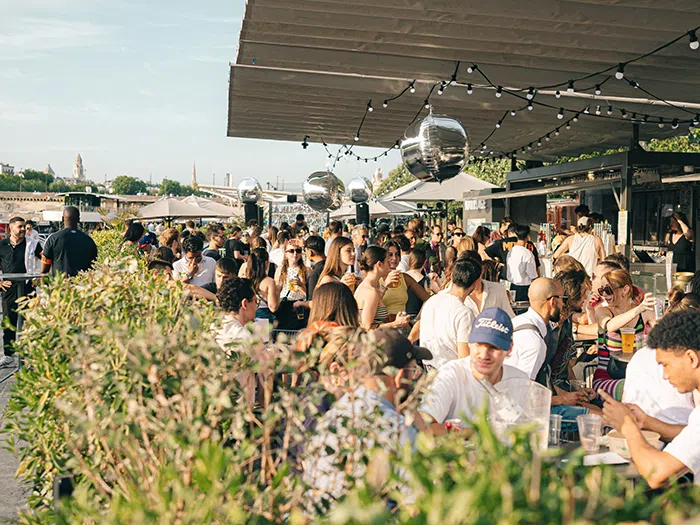 A crowd at a lively outdoor bar by the river.