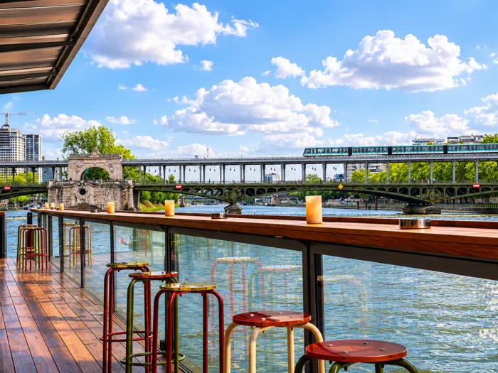 Terrace with view of bridge over river, old building in the background.